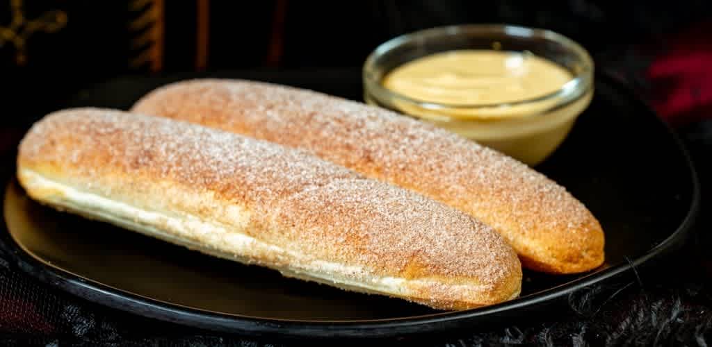 Two golden breaded fish filets with a side of creamy tartar sauce on a black plate