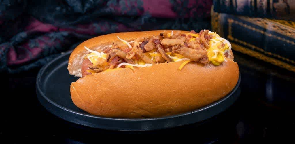 A hot meatball sandwich with melted cheese and cooked bacon in a toasted bun on a black plate