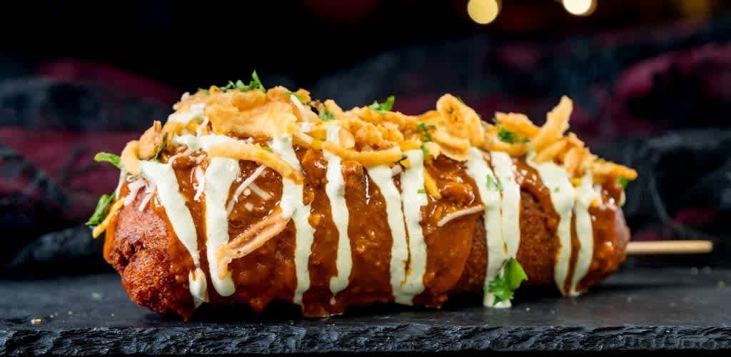 Fried food item topped with sauce, shredded cheese, and crispy strips on a dark surface with a blurred background