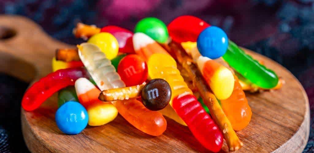 Assorted colorful gummy worms and candies on a round wooden board.