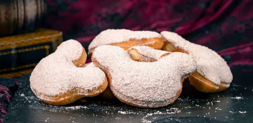 Three sugar-dusted cookies with a heart shape and a creamy filling on a dark surface with a colorful background.