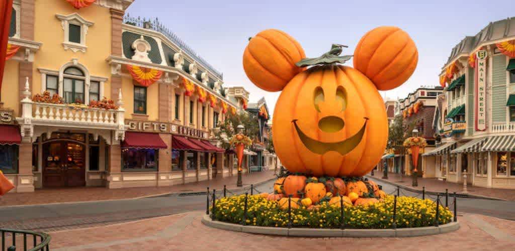 Large pumpkin decoration featuring Mickey Mouse ears and a smiling face at a Disney park during fall season with autumnal decorations