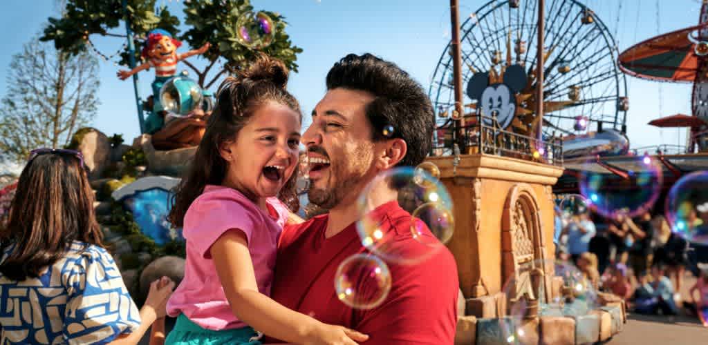 A happy father and daughter are enjoying a day at an amusement park with bubbles, rides, and bright attractions in the background