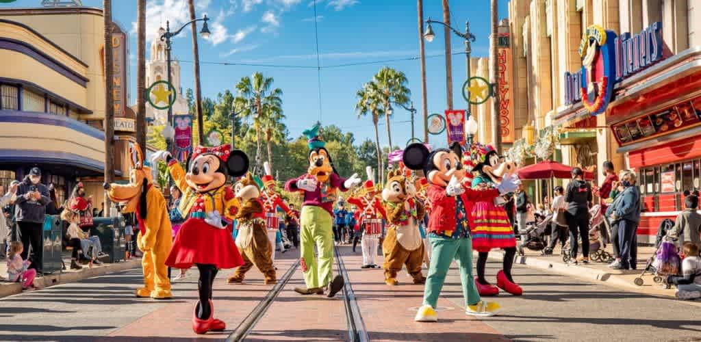 Disney characters including Mickey and Minnie Mouse parade down a lively street filled with spectators and colorful decorations under a bright blue sky
