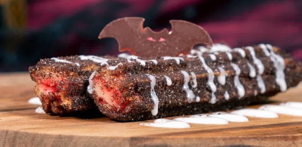 Chocolate cake with white icing drizzles and a decorative bat-shaped chocolate topper on a wooden surface
