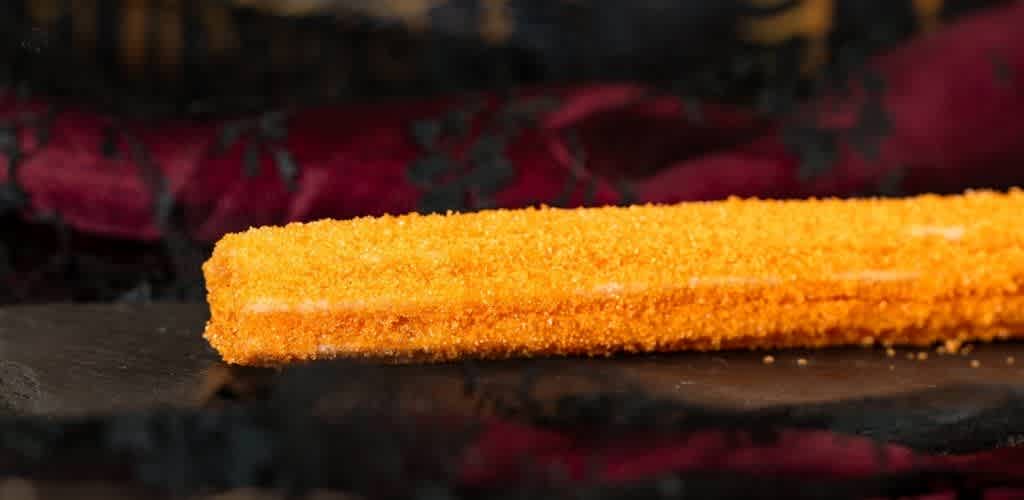 A golden-brown breaded fish fillet resting on a dark surface with a blurred colorful background