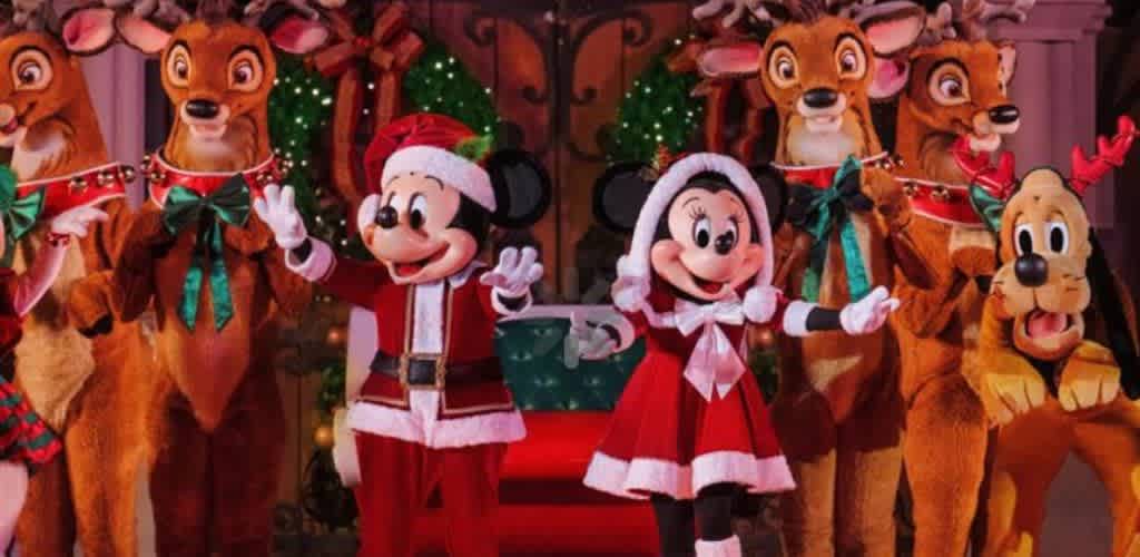 Mickey and Minnie Mouse dressed in Christmas costumes with Santa hats, surrounded by Disney characters in a festive holiday setting with decorated trees and ornaments.