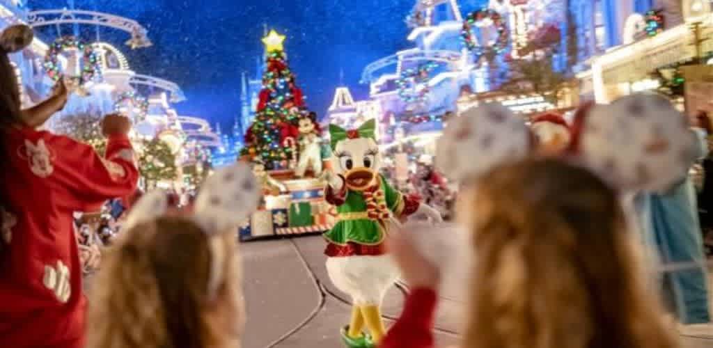 Disney characters in Christmas costumes greeting children at a festive holiday event with decorated buildings and a Christmas tree.