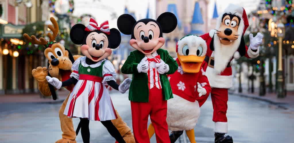Group of people dressed as Disney holiday characters including Mickey Mouse Minnie Mouse Donald Duck Goofy and Pluto standing outside on a festive streetalking to the camera