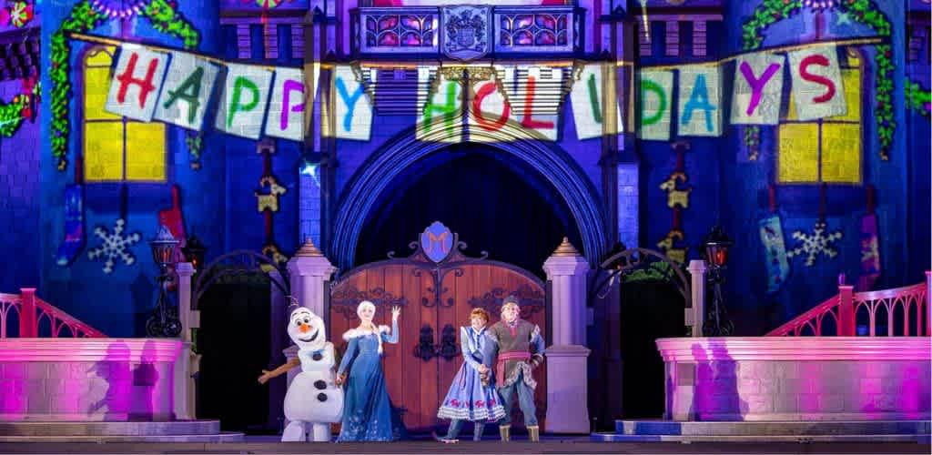 The image shows a colorful stage with characters from Frozen standing in front of a castle with a holiday banner reading Celebrating holidays
