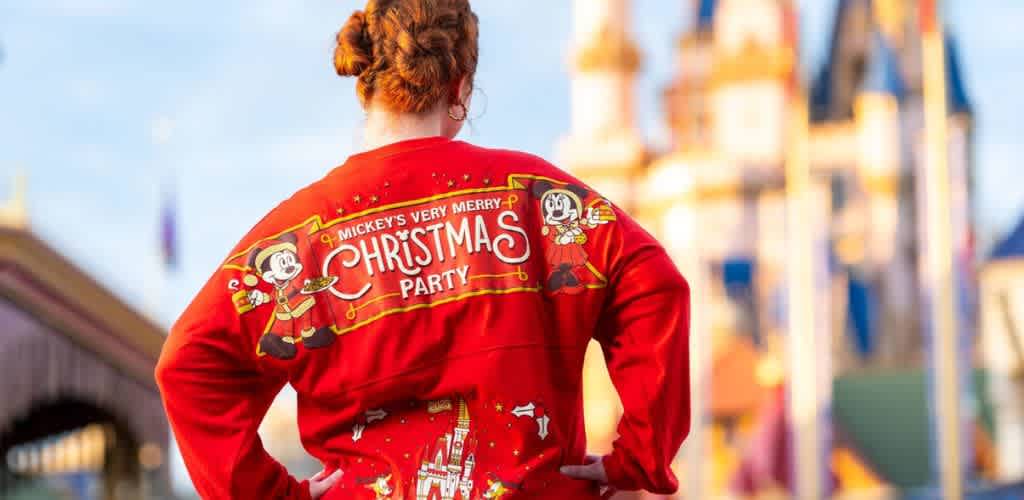 Person wearing a red holiday sweater with Mickey Mouse and Christmas decorations at an amusement park
