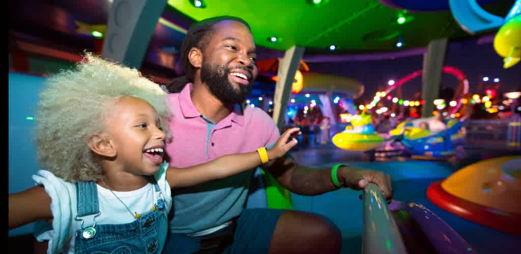 A smiling man and young girl enjoying a colorful amusement park ride with bright lights and vibrant colors in the background
