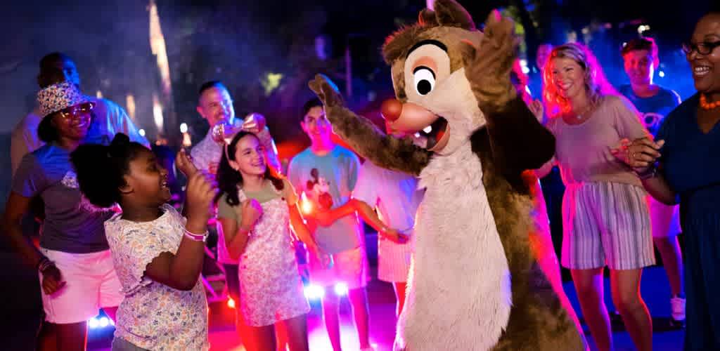 A group of children and adults dancing happily with a person in a chipmunk costume at a colorful party.