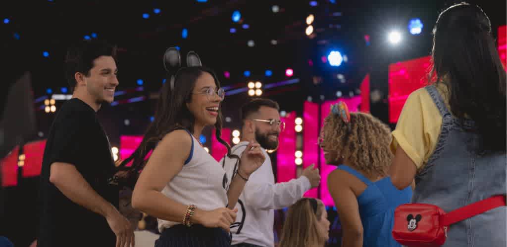 Group of diverse people enjoying a lively event with colorful lights and cheerful expressions.