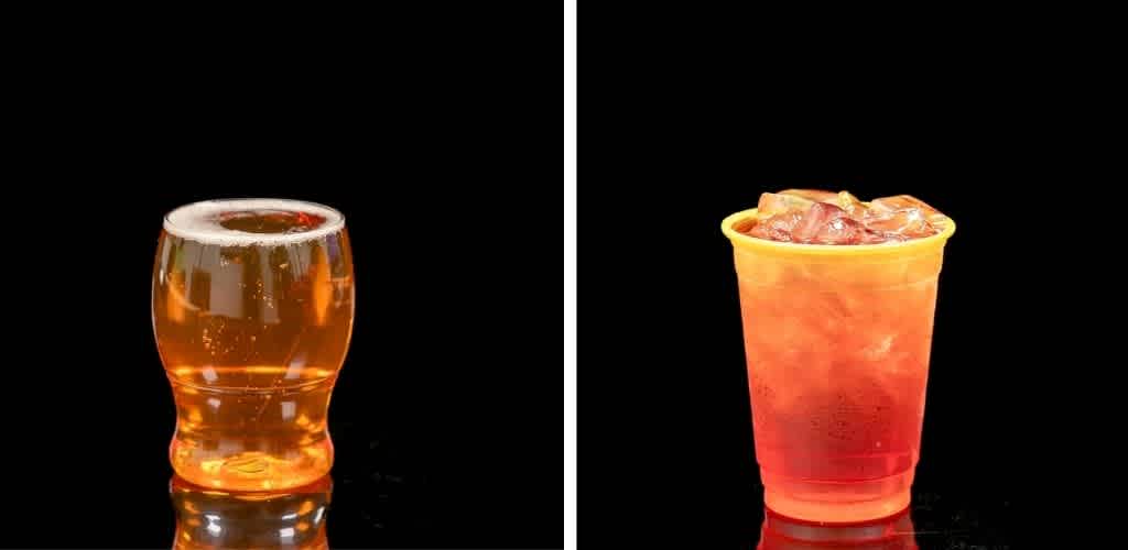 A clear glass of beer and a yellow cup of iced tea on a black background