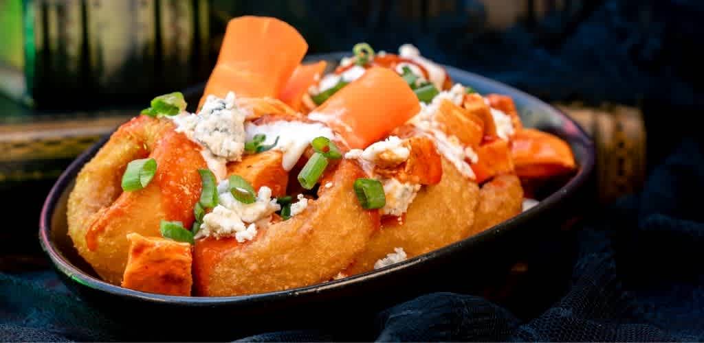 A bowl of crispy fried chicken topped with orange sweet potato chunks, blue cheese crumbles, chopped green onions, and drizzled with sauce.