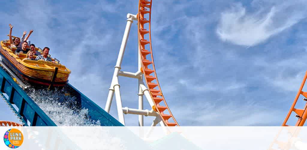 People on a descending water coaster at an amusement park with a roller coaster in the background.