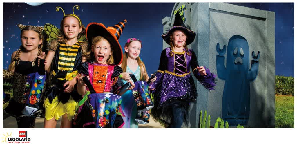 Children in Halloween costumes holding candy bags next to a tombstone with a painted ghost.