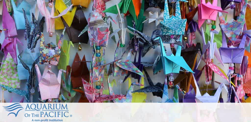 A vibrant display of colorful origami cranes with the Aquarium of the Pacific logo below.