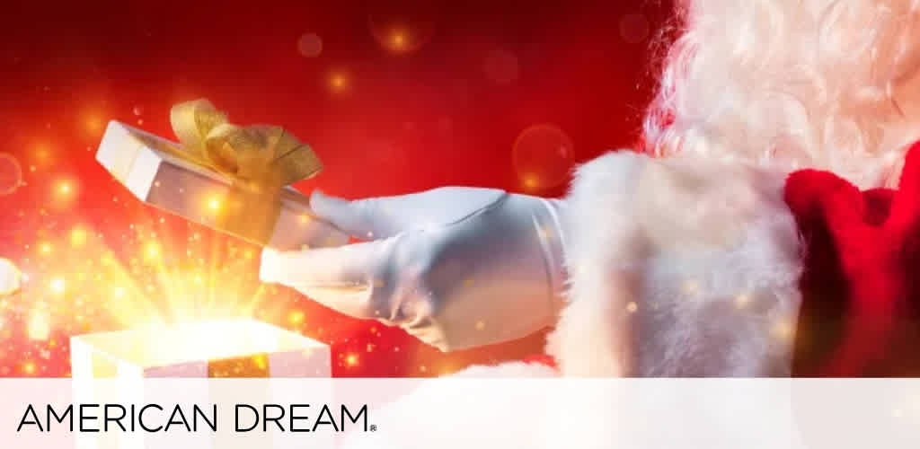 Santa Claus holding a white gift box with a glowing light and gold ribbon against a festive red background.