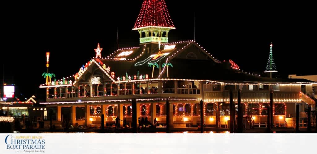 A brightly decorated, illuminated building with a tower, palm trees, and festive lights at night, representing a holiday-themed event or attraction.