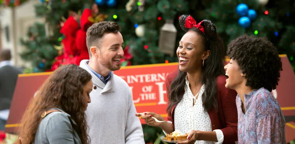 Four people smiling and enjoying a holiday celebration in front of a decorated Christmas tree