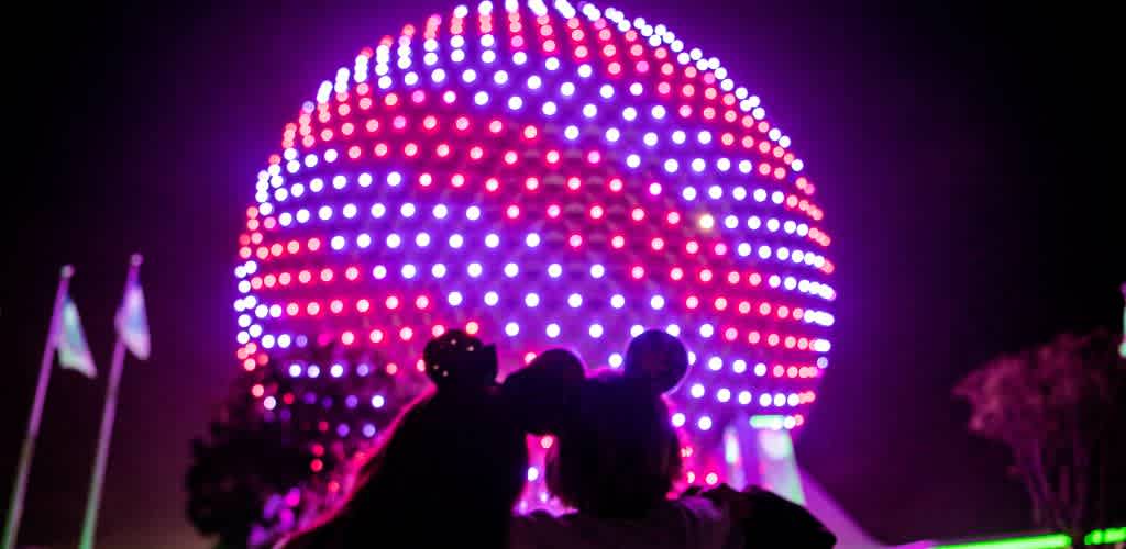 Silhouettes of two people looking at a brightly lit spherical structure at night with colorful illuminated dots.