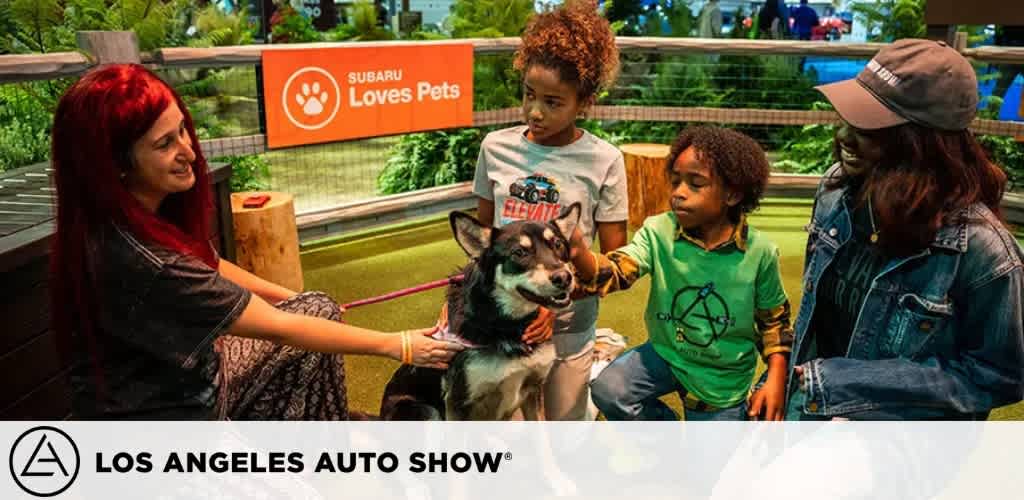 People petting a dog at the Los Angeles Auto Show with a sign reading 
