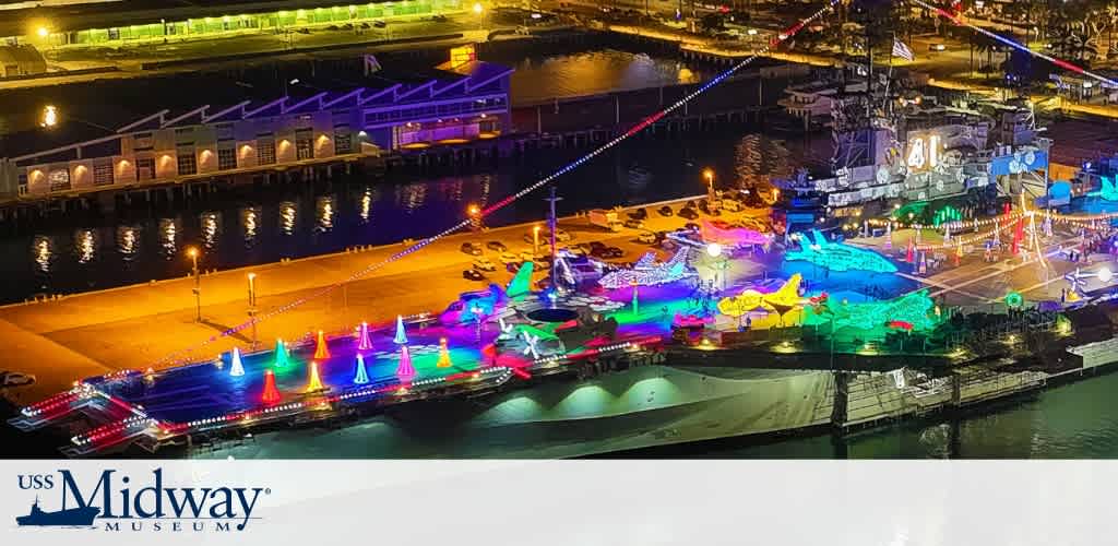 Aerial night view of the USS Midway Museum decorated with colorful holiday lights.