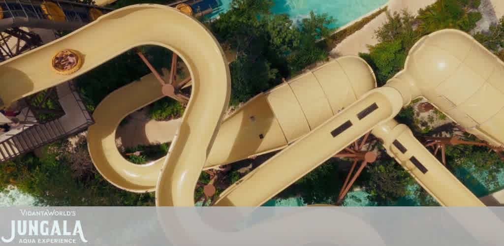 A large beige water slide with twists and turns, surrounded by green trees and a pool area, viewed from above.