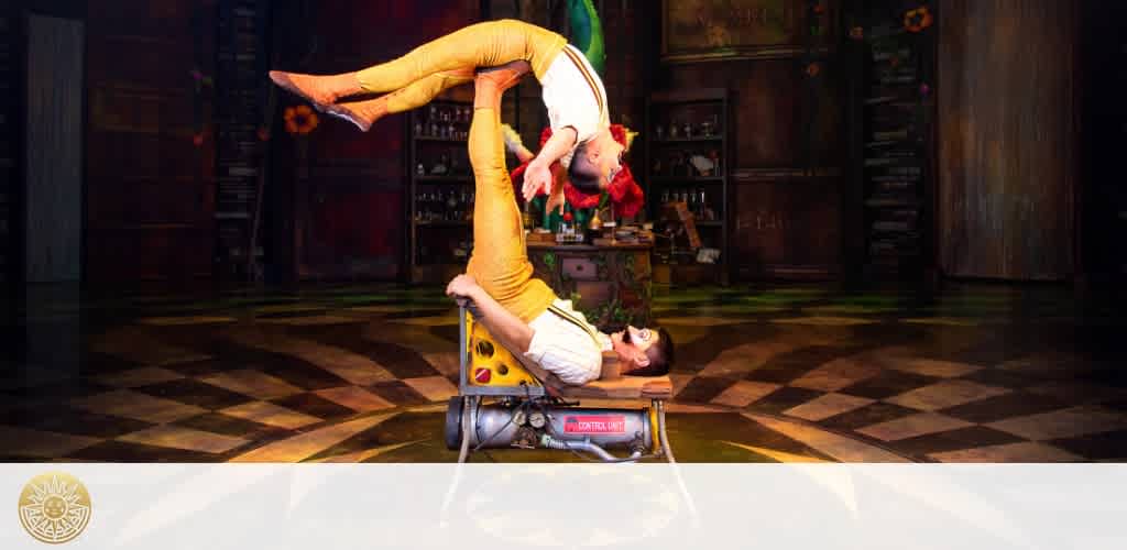 A male performer balances a female performer upside down on his feet during a circus act in a wooden-floored performance space.