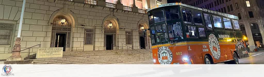 A city bus parked on a street in front of a historic building with steps and arched entrances at night