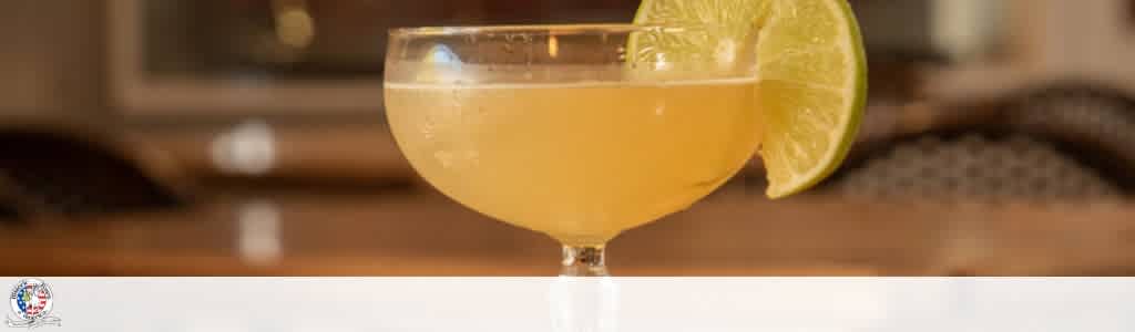 A cocktail in a stemmed glass garnished with a lemon wedge on the rim