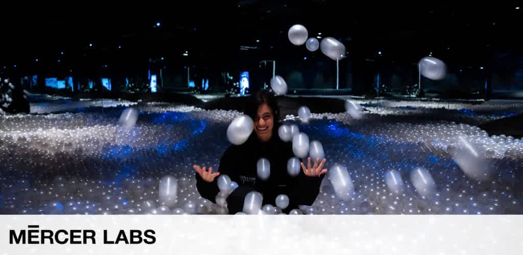 Person smiling amidst an interactive display of floating illuminated spheres in a dark environment at Mercer Labs