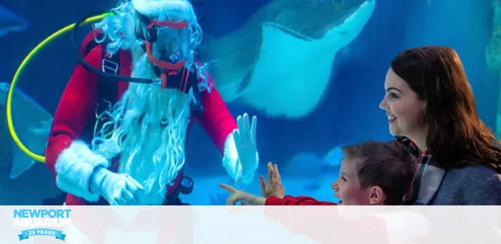 Santa Claus scuba diving in an aquarium tank, interacting with a woman and child through the glass.