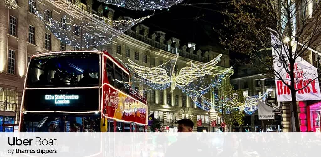 A red double-decker bus in London under festive holiday lights shaped like wings.