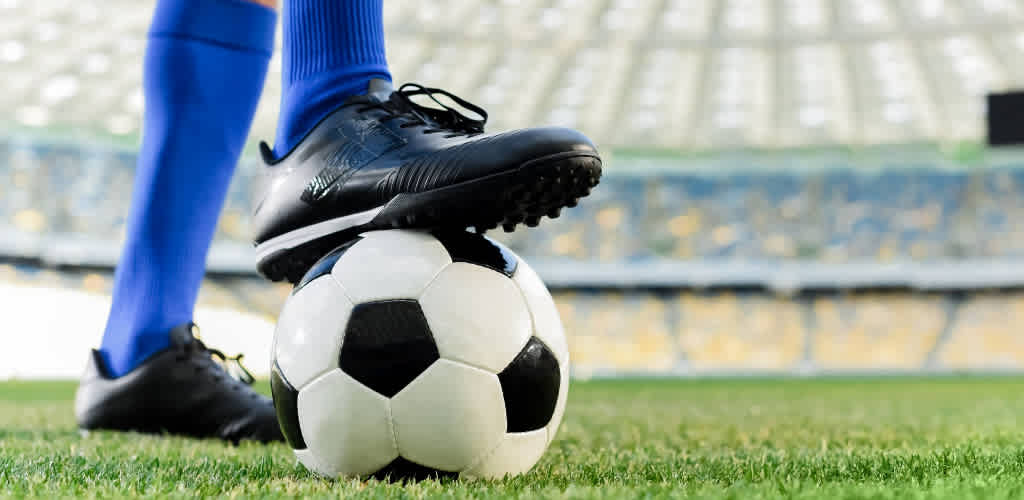 A soccer player wearing blue socks and black shoes balances a soccer ball on the grass field.