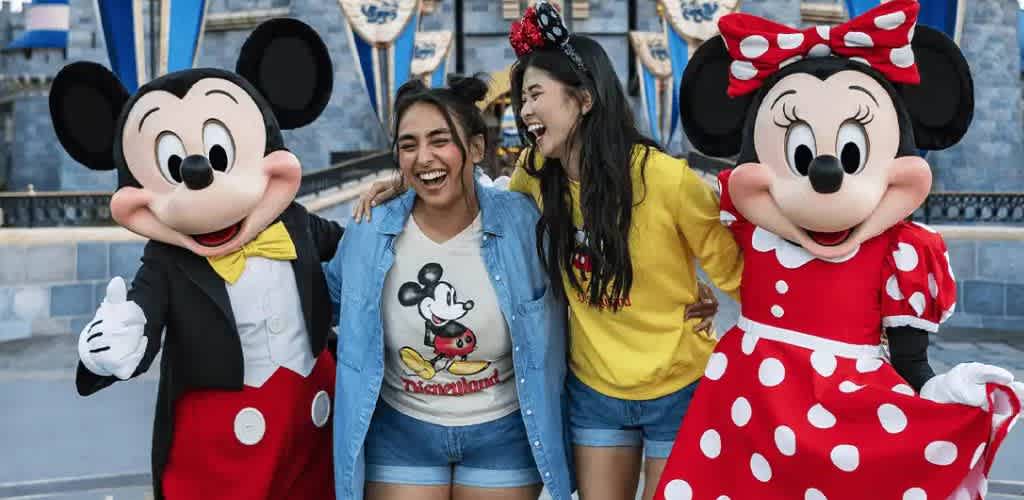 Two women smile and embrace Disney characters Mickey Mouse and Minnie Mouse at an amusement park