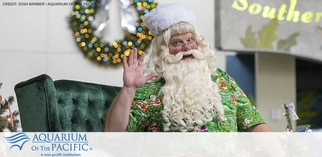 Santa Claus wearing a Hawaiian shirt waves while sitting in a green chair with holiday decor in the background.