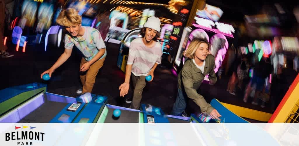 Three young people playing skee ball at an arcade with vibrant lights and energetic atmosphere.