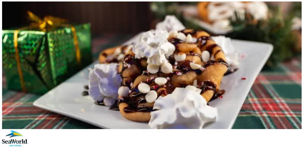 A funnel cake topped with white chocolate chips, chocolate drizzle, and whipped cream on a white plate with a festive background.