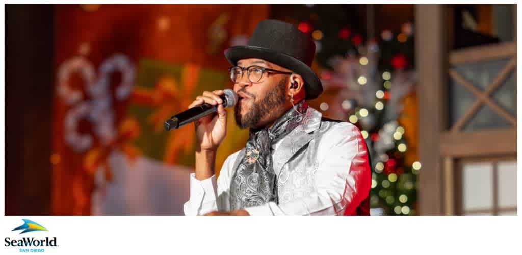 A performer in a black hat and silver vest sings into a microphone with a festive, blurry holiday-themed background. SeaWorld San Diego logo at the bottom.