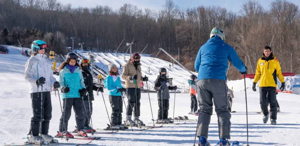 Group of people learning to ski on a snowy slope with instructors on a bright winter day
