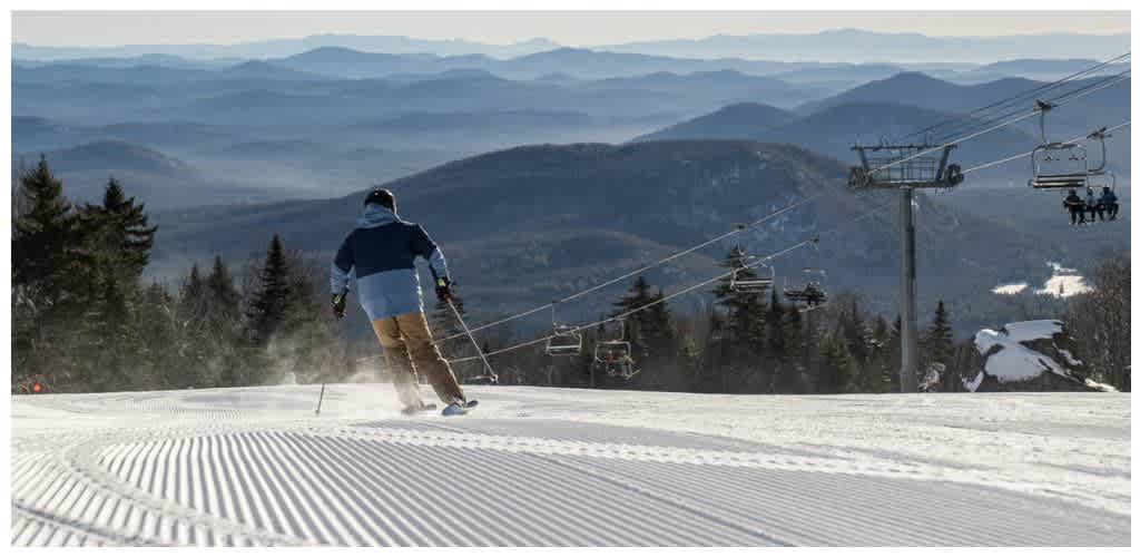 A person skiing down a snowy slope with a ski lift and mountain landscape in the background