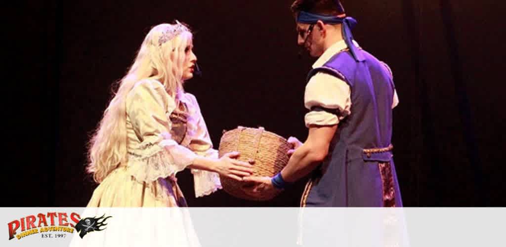 Two performers in costume on stage, with a woman in a cream gown and a man in a blue pirate outfit sharing a basket.