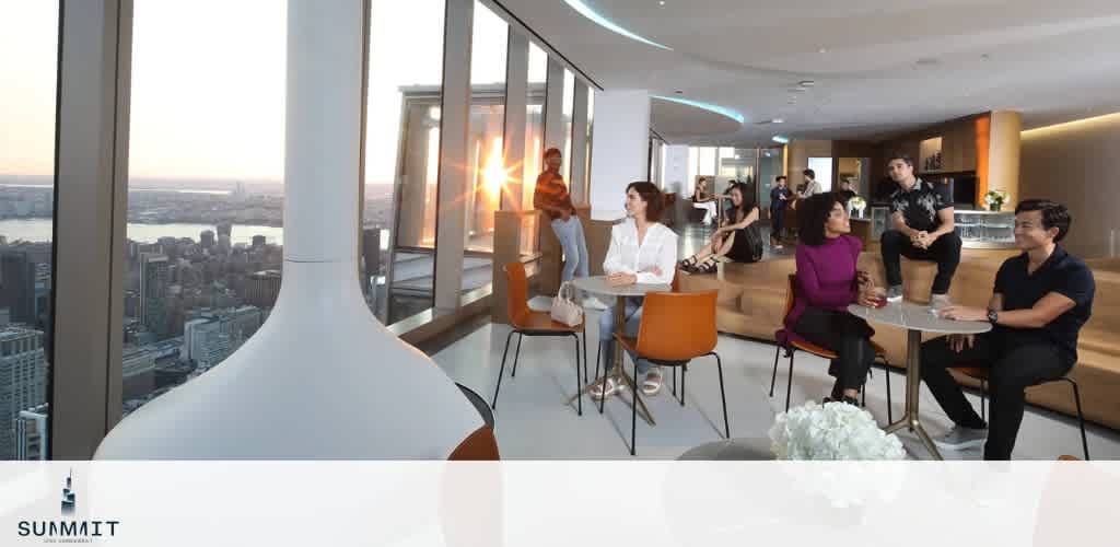 A modern lounge with large windows offering a city view, people seated at tables.