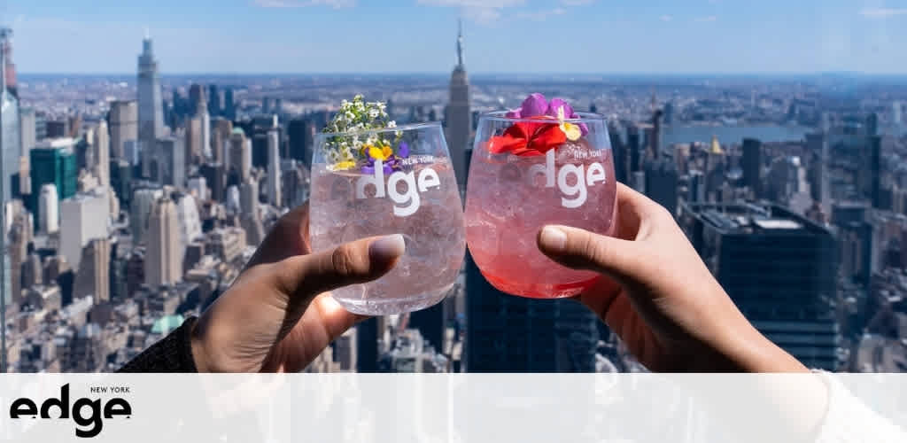 Two hands hold garnished cocktails with the New York City skyline in the background.