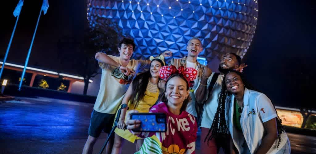 Group of diverse friends taking a fun selfie at night in front of spaceship Earth at Epcot Orlando Disney World.