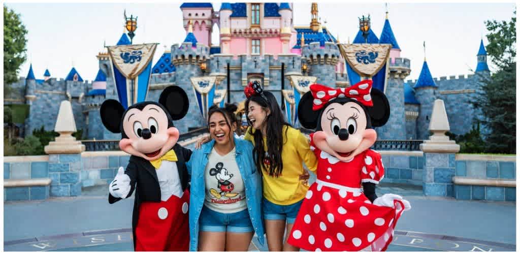 Two women smile with Mickey and Minnie Mouse characters in front of Sleeping Beauty Castle at Disneyland