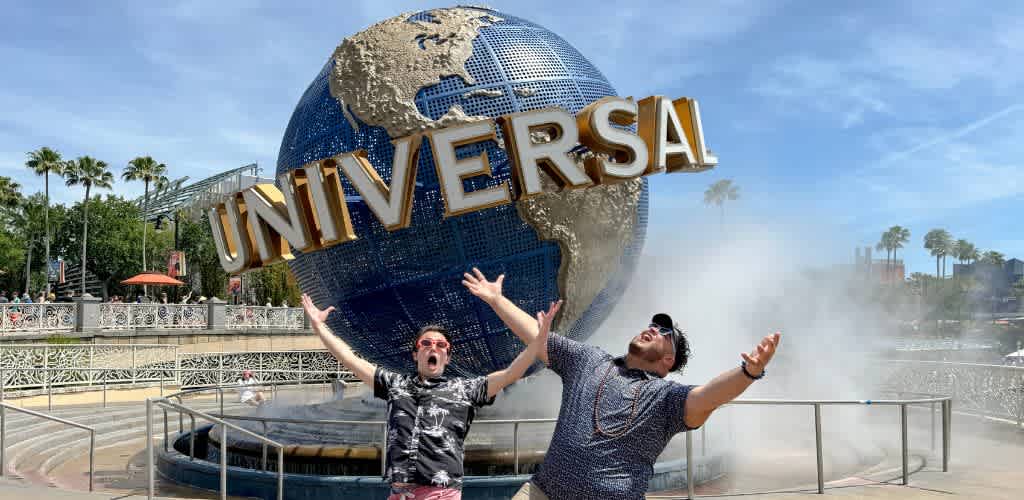 Two people standing in front of the Universal Studios globe at Universal Studios theme park with arms raised and smiling.